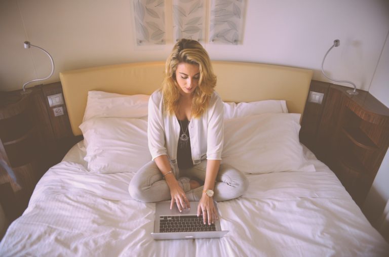 middle aged woman scrolling through laptop on bed