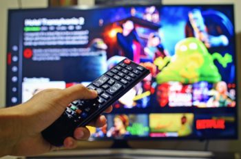 hand controlling remote with netflix on the tv in the background